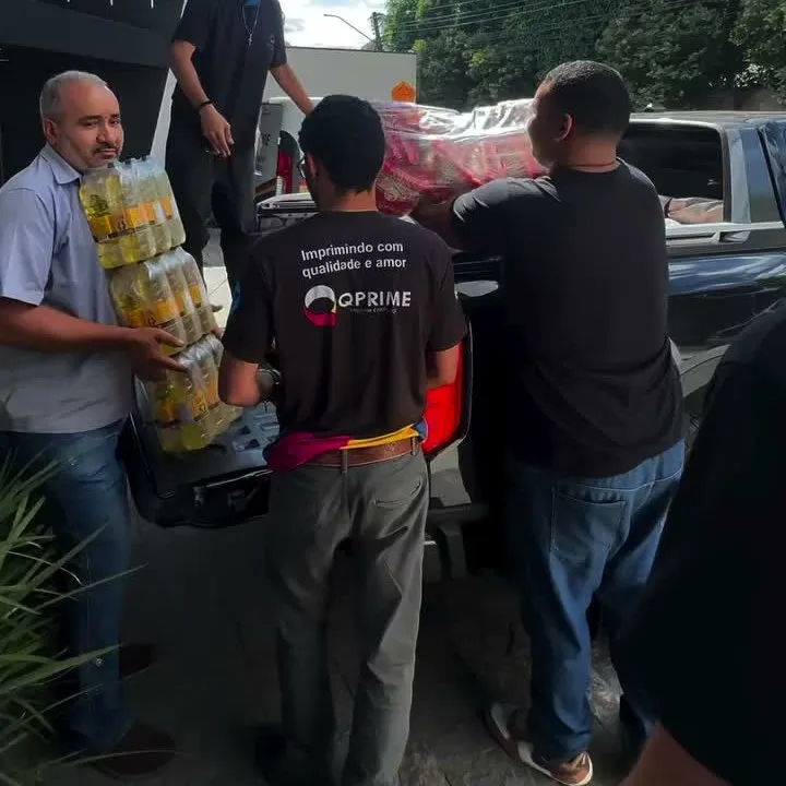 Funcionários da QPrime carregando cestas básicas e óleo para a caçamba de uma caminhonete, na entrada da empresa.