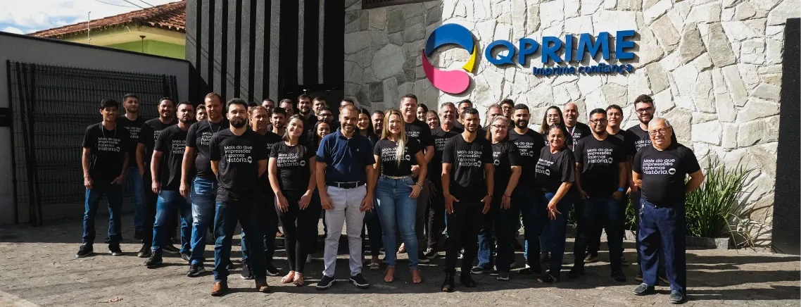 A equipe da QPrime reunida na entrada da sede, sob o letreiro da empresa.