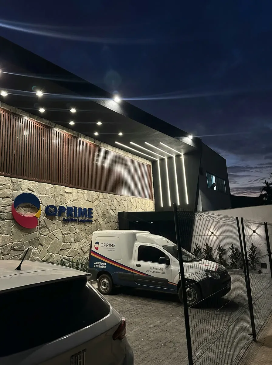 A fachada da sede da QPrime iluminada ao anoitecer, com uma van da frota estacionada na entrada.
